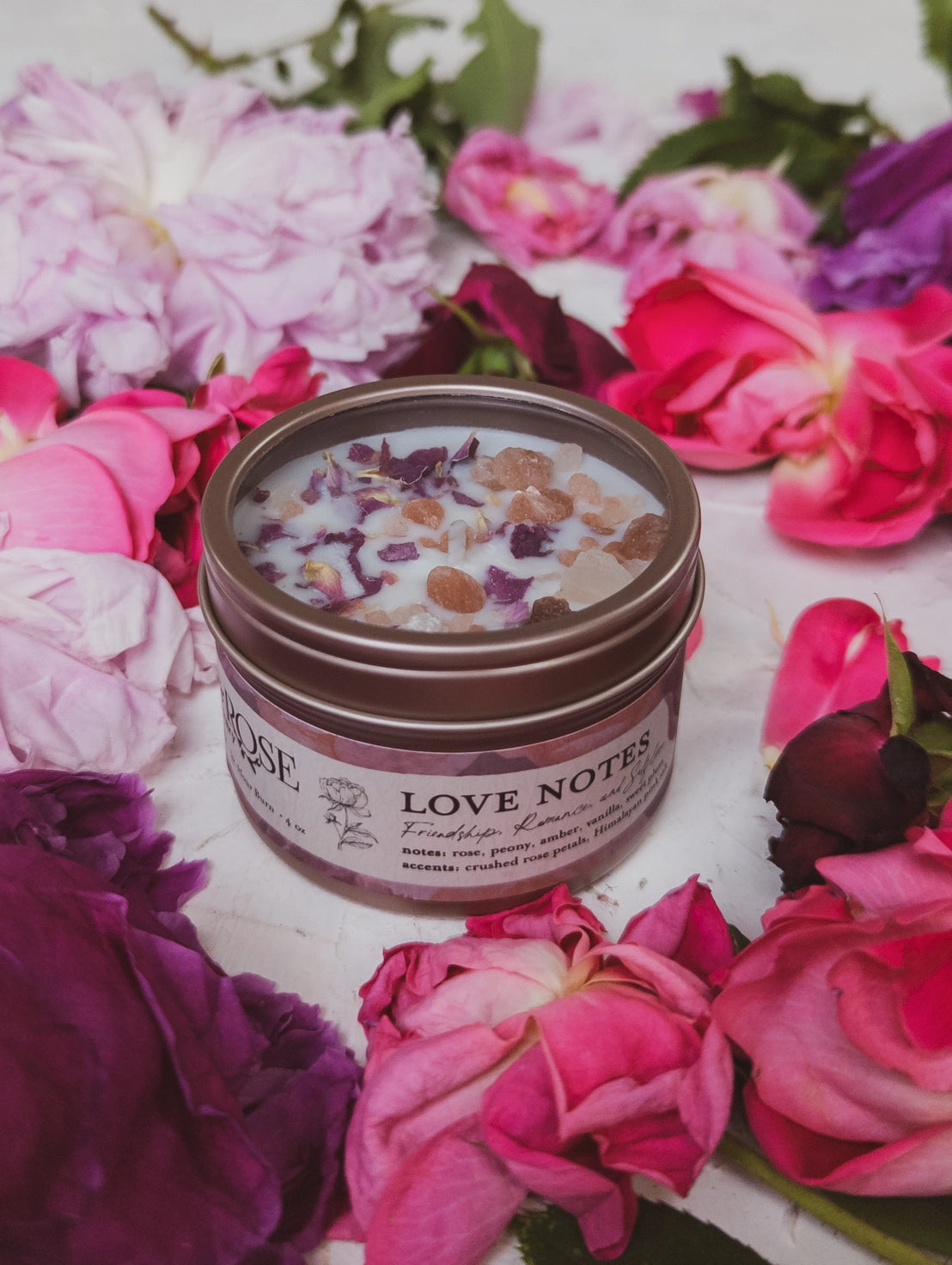 Jar of 'Love Notes' candle surrounded by pink and purple flowers