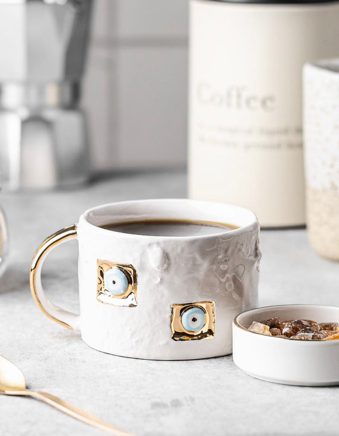 White ceramic mug with gold accents on a kitchen counter with coffee and cereal.