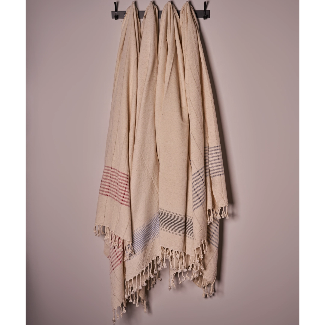 Beige towel with fringe details hanging on a rack against a plain background