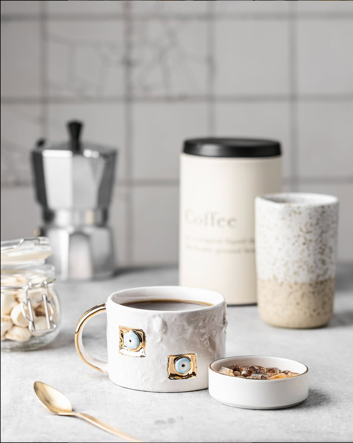 Ceramic mug with decorative elements on a kitchen counter with coffee beans and a coffee grinder.