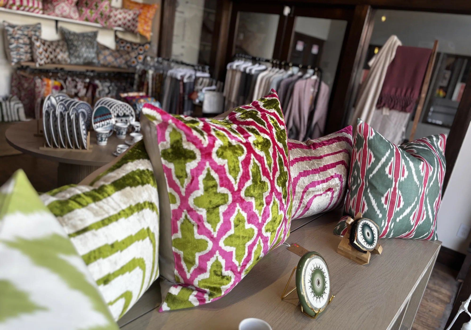 Decorative pillows with green and pink patterns on a wooden surface in a store setting.