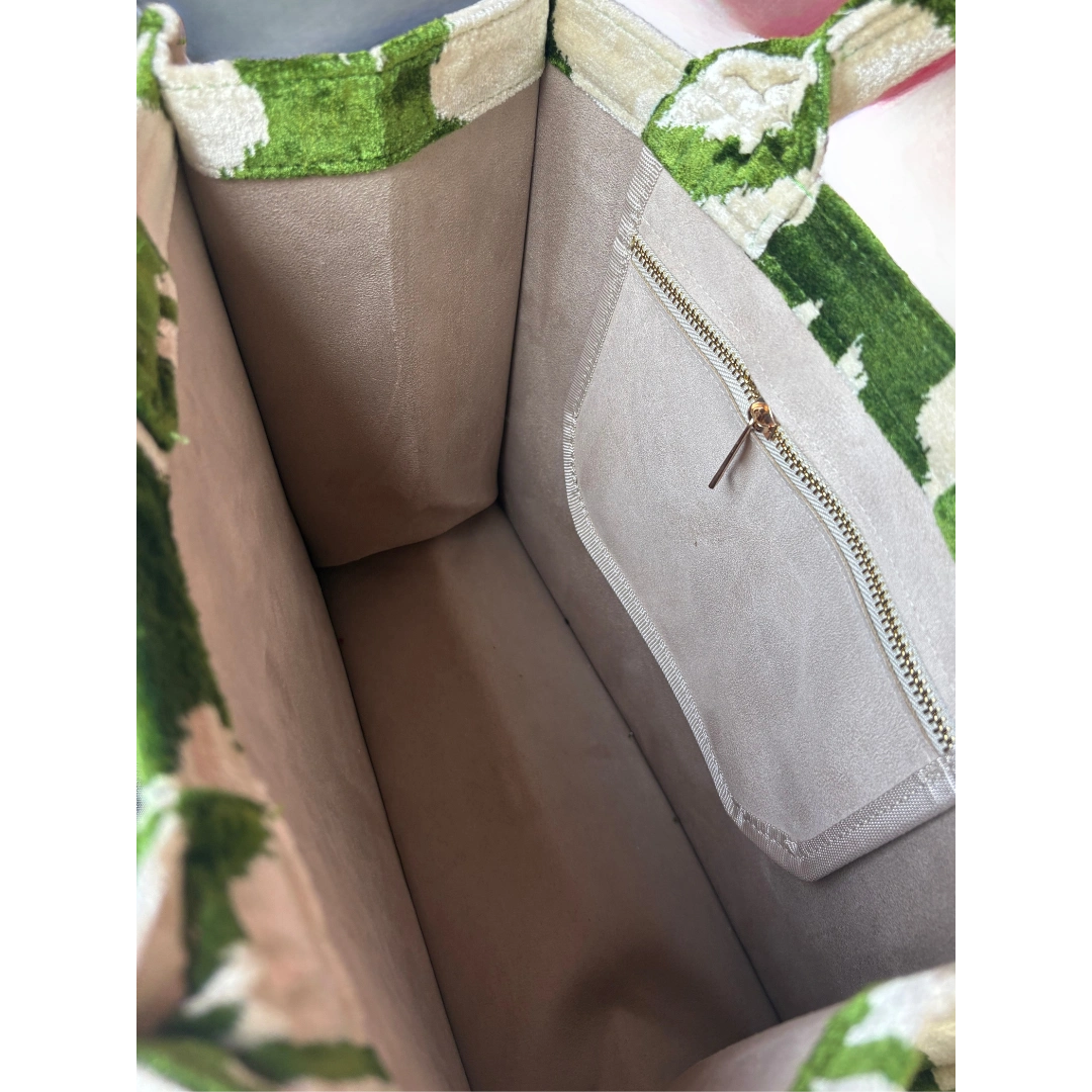 Close-up of a beige handbag with green floral pattern on a white background