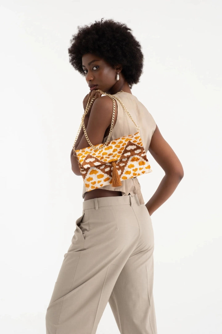 Model in a tan waistcoat and trousers holding the amber leopard silk velvet clutch