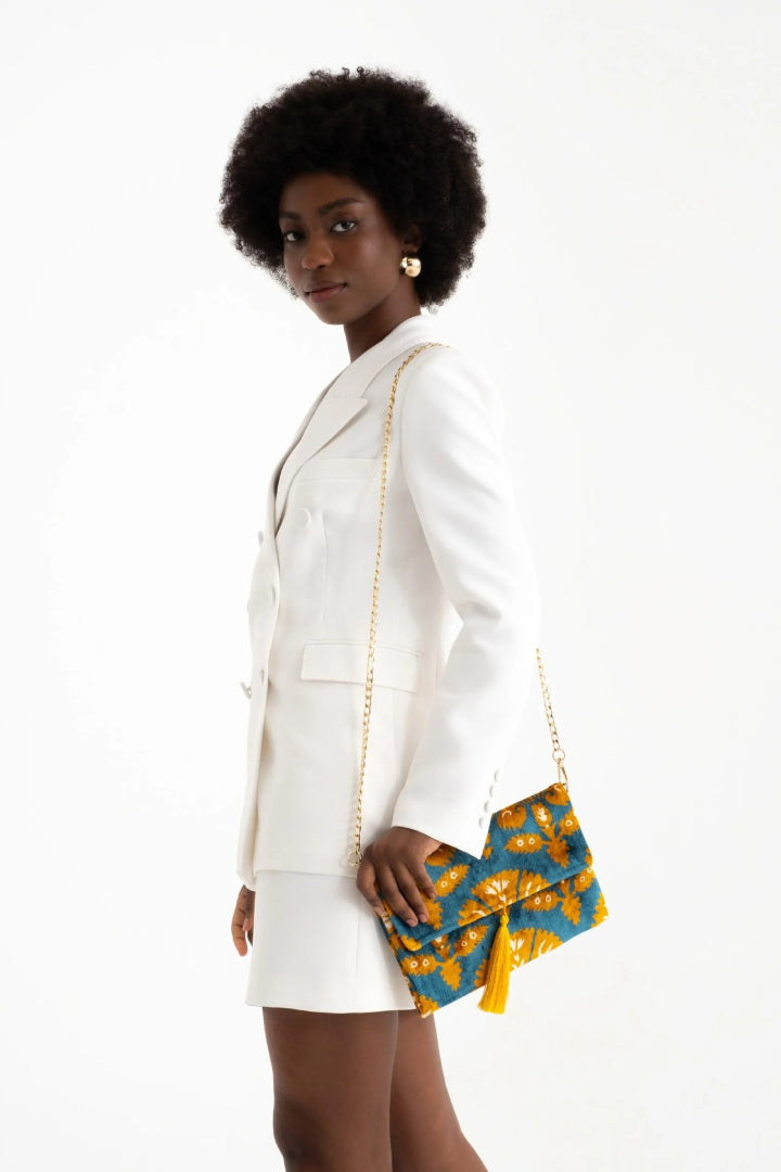 The azure and saffron Fiori silk velvet clutch held against a white tailored outfit