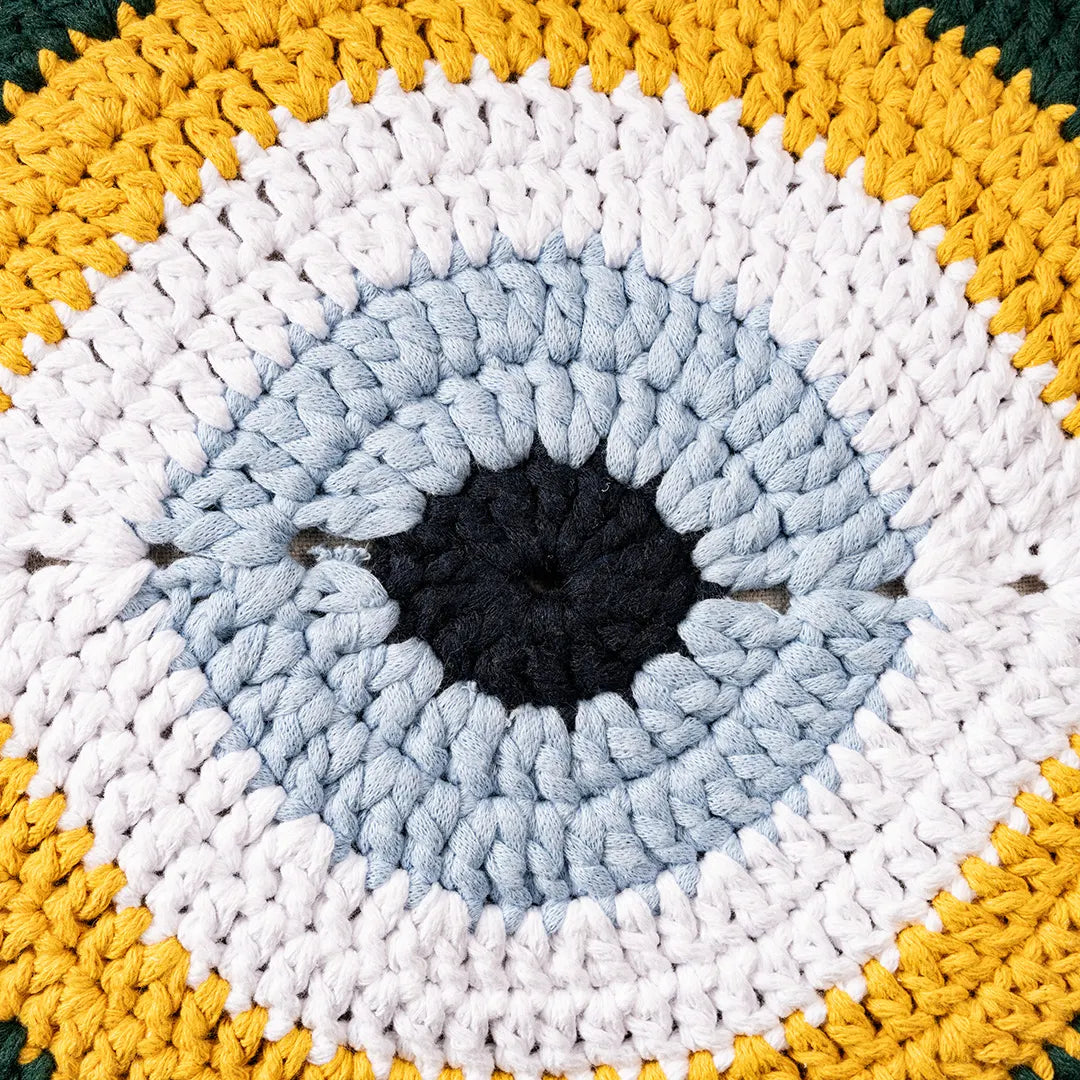 Close-up of the gold and green crocheted evil eye motif with its pale blue iris