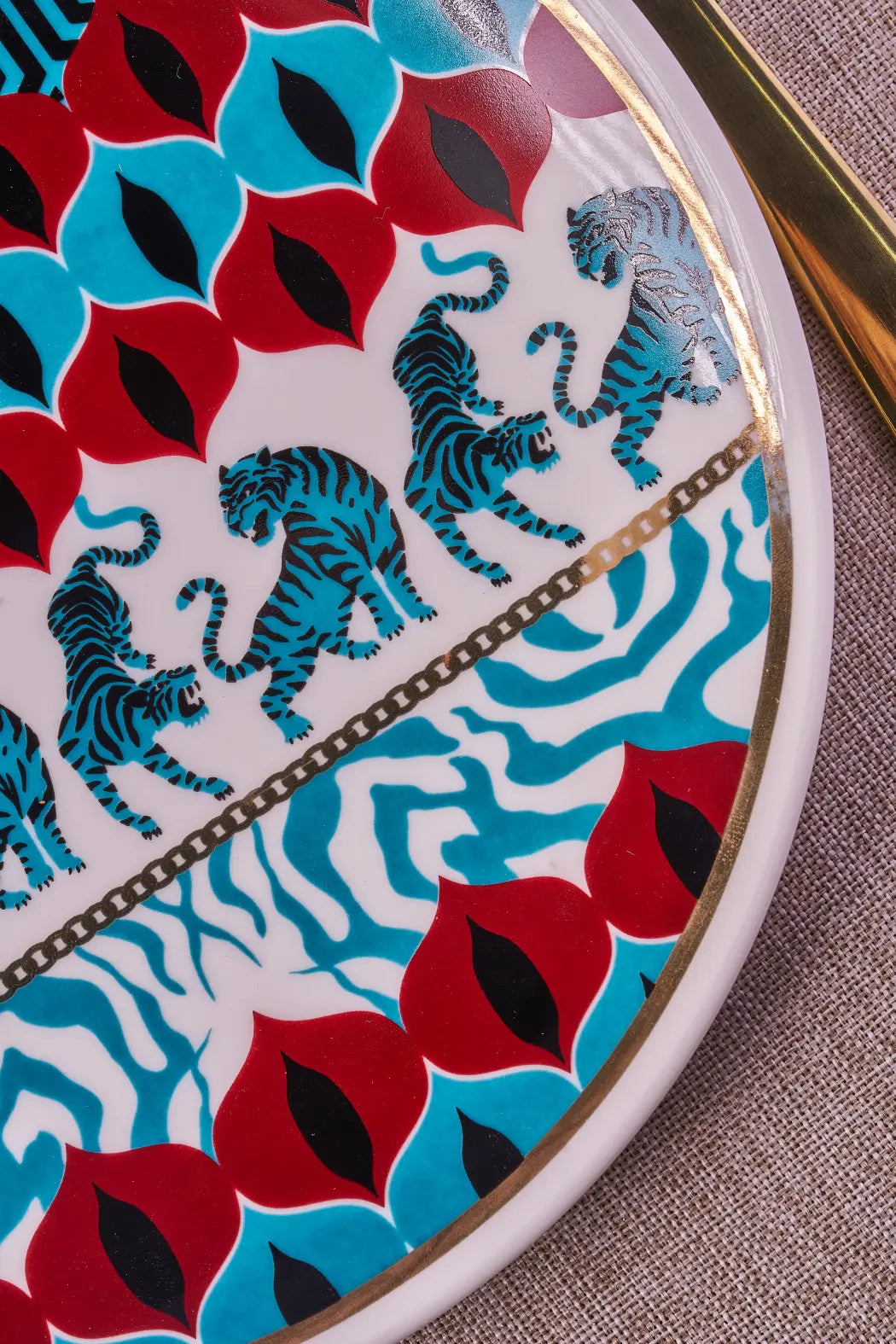 Close-up of the Gatto Wild plate pattern: turquoise tigers, red and blue leaf motifs, zebra stripes and a gold chain line