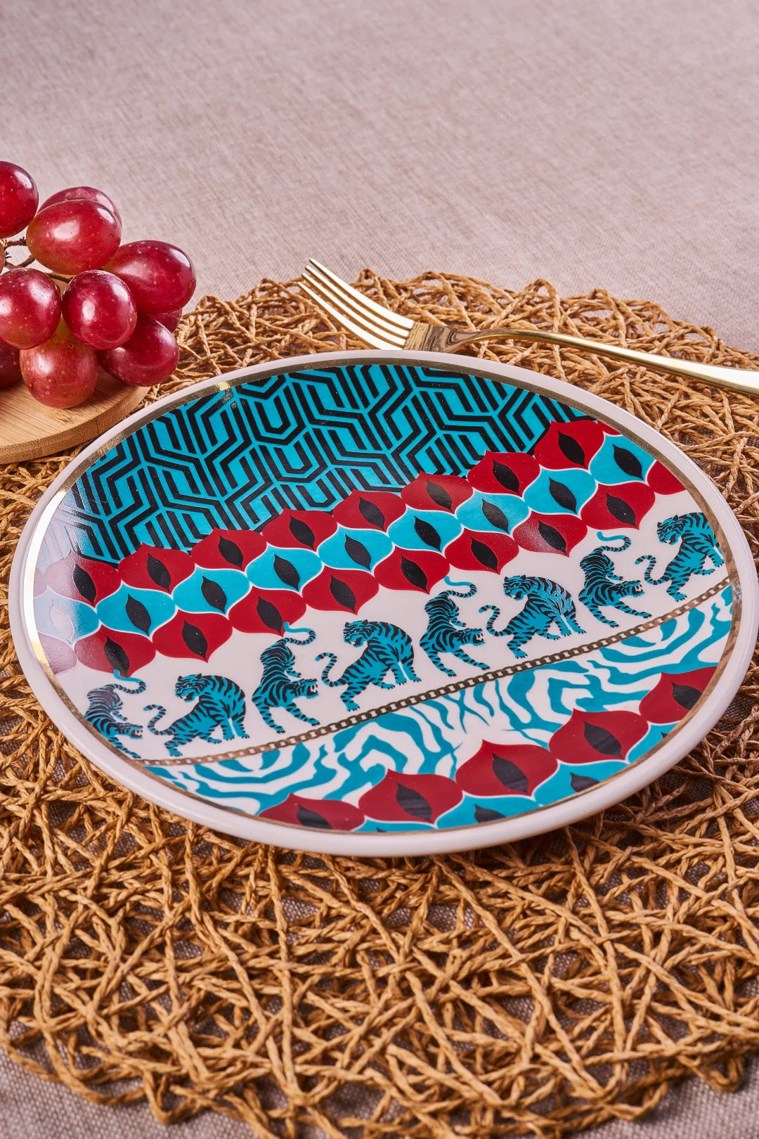 Gatto Wild 9-inch porcelain plate with a band of tigers and a gold rim, styled on a woven placemat with red grapes