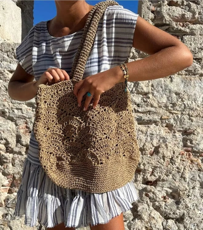 Woman in a striped dress carrying the Cristina raffia tote on her shoulder at the beach