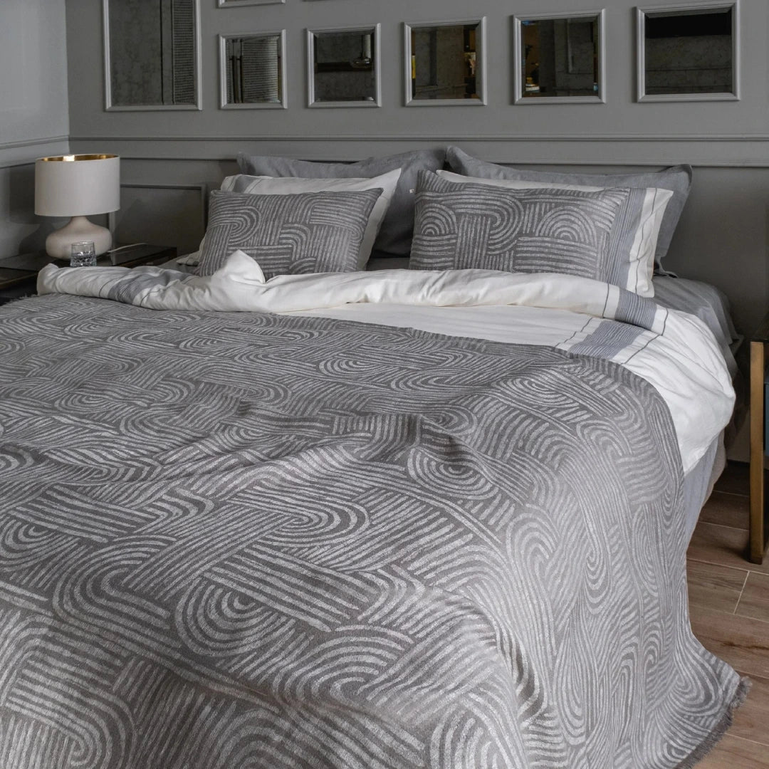 Bed with gray and white patterned bedding in a bedroom setting.