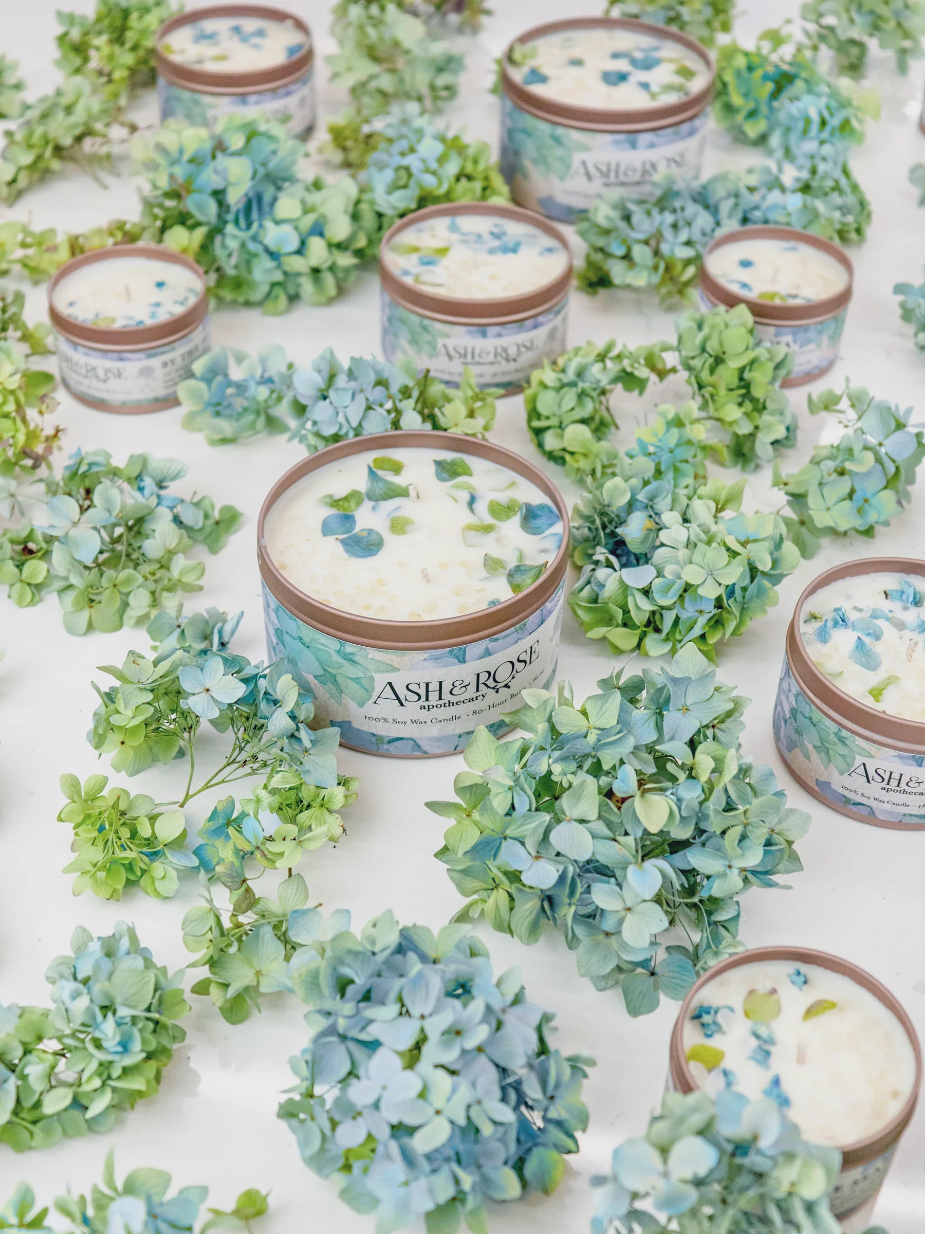 Candles with floral designs on a white surface surrounded by green and blue flowers