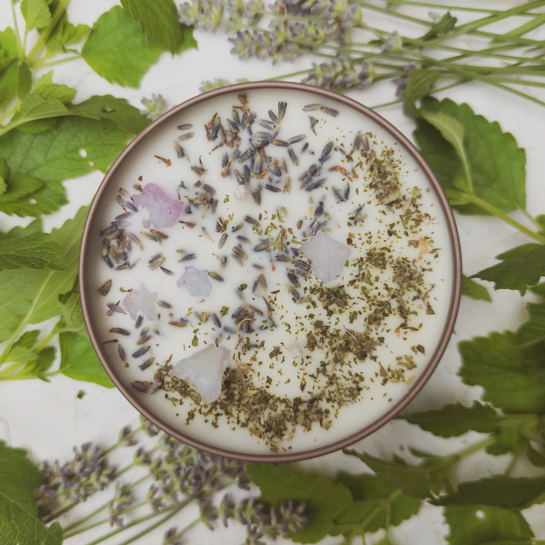 Top-down view of a bowl with dried herbs and flowers on a white background with green leaves and lavender.