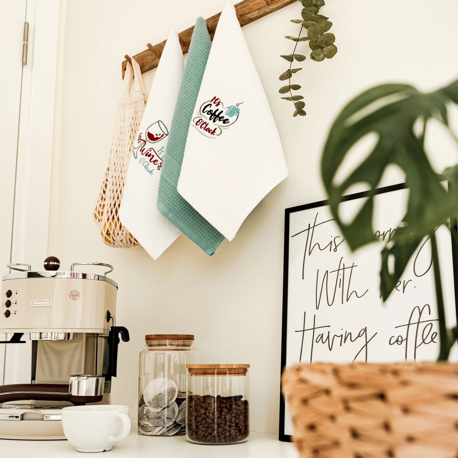 Kitchen counter with coffee machine, jars, and decorative items including a framed quote and hanging towels.