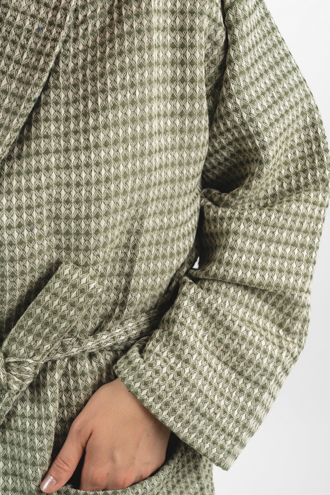 Close-up of a green and beige checkered coat with a hand wearing a ring on a white background