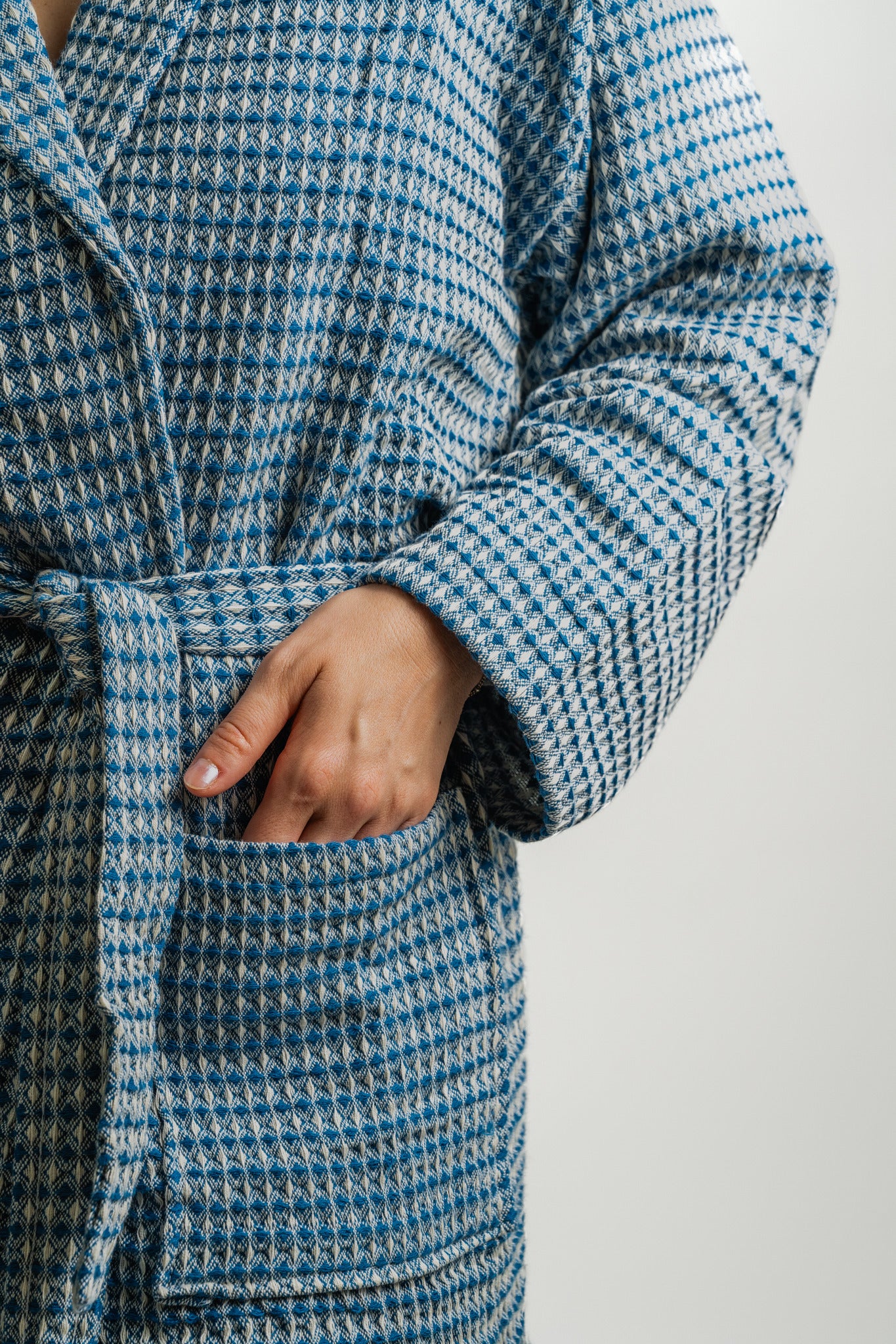 Blue and white checkered coat with a hand in the pocket on a light gray background