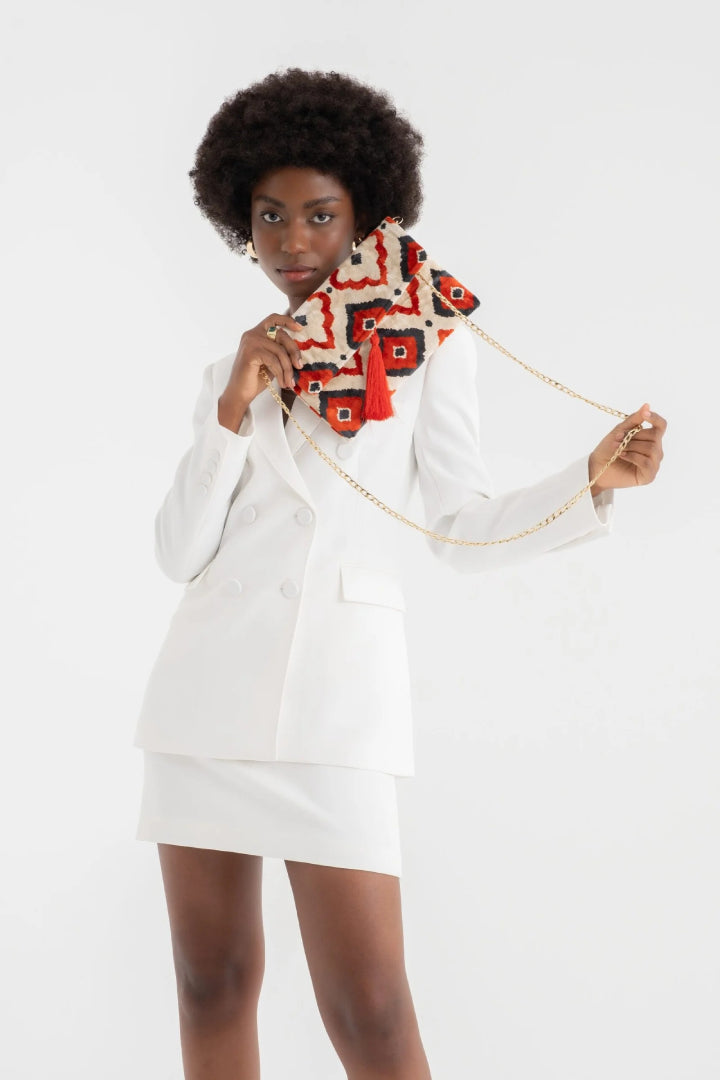 The rust ikat diamond silk velvet clutch carried by its tassel against a white outfit