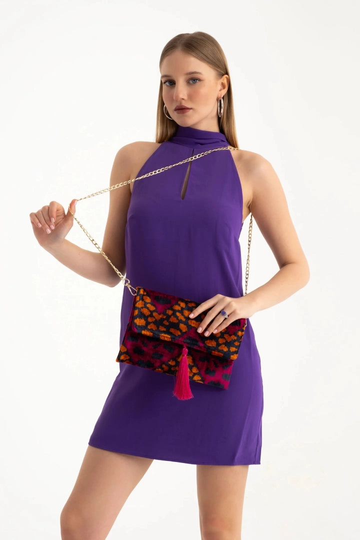 The berry leopard silk velvet clutch carried by its tassel against a purple dress