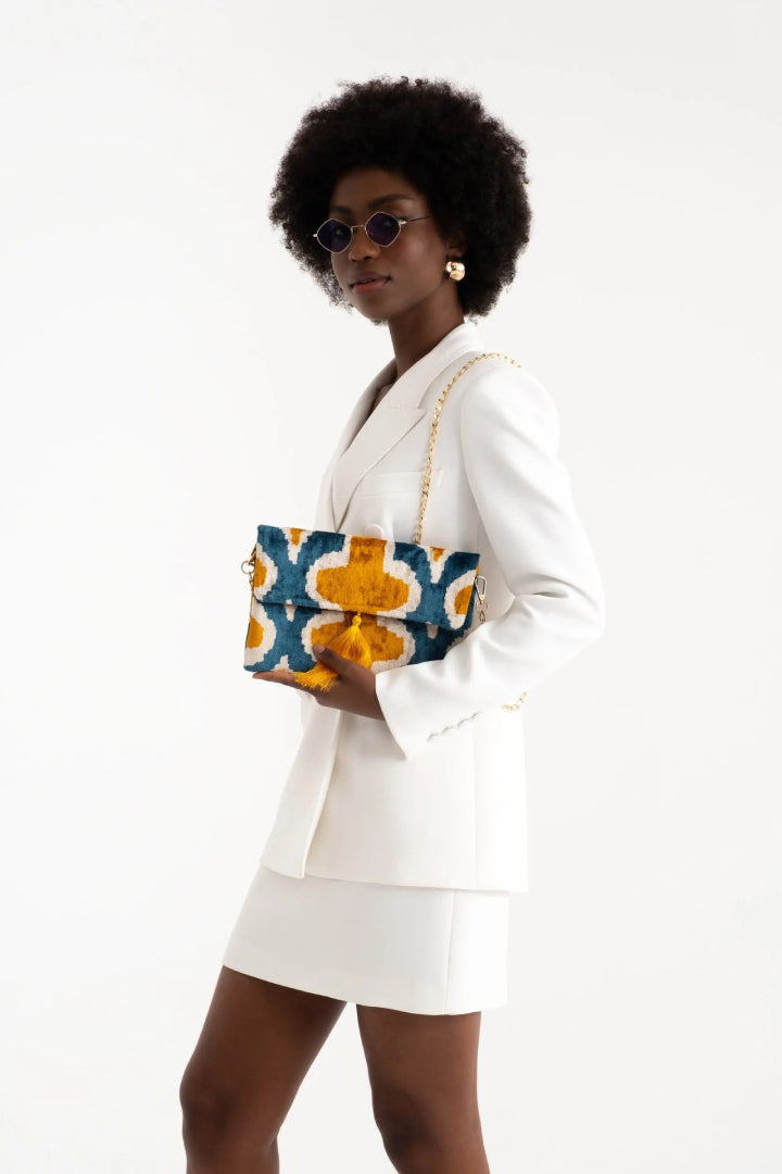 The teal and saffron quatrefoil silk velvet clutch held against a white outfit