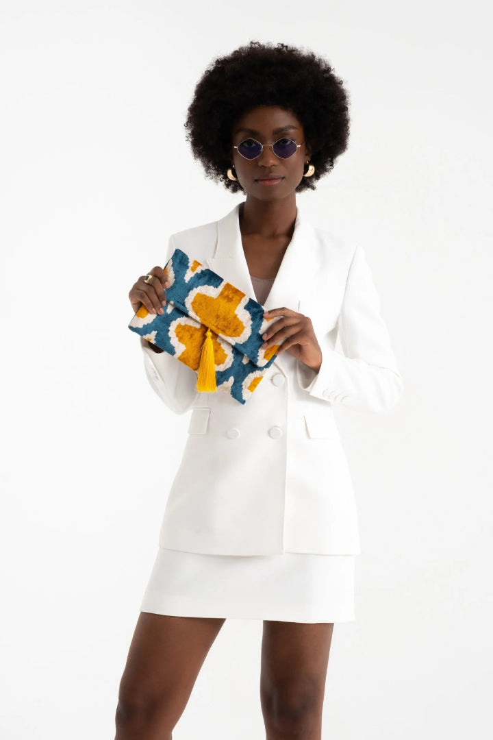 Model in a white blazer dress holding the teal and saffron silk velvet clutch