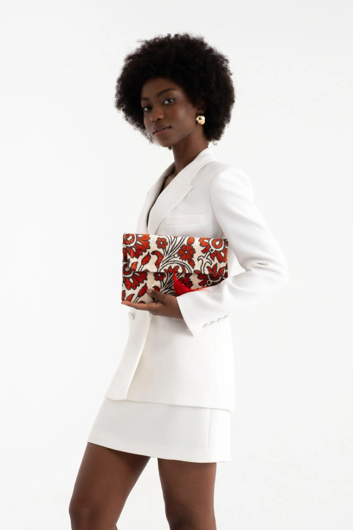 Model in a white blazer dress holding the coral carnation silk velvet clutch