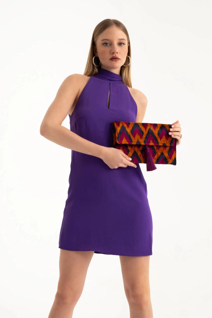 Model in a purple dress holding the chevron silk velvet clutch at the waist