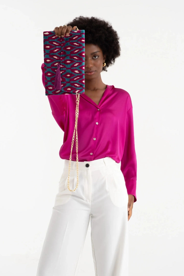 The berry and turquoise rana petal silk velvet clutch held up by its tassel