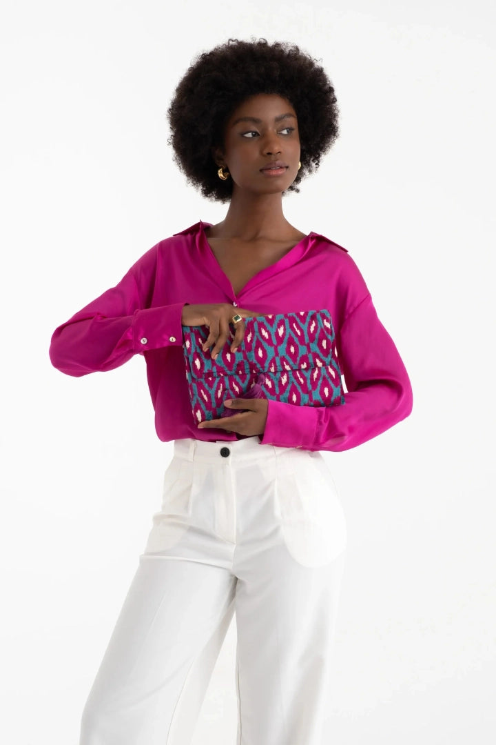 Model in a fuchsia shirt holding the berry and turquoise rana petal clutch