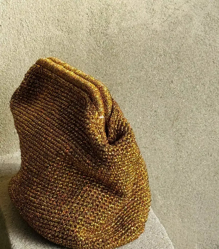 Side view of the gold Sabine metallic crochet clutch showing its pleated shape