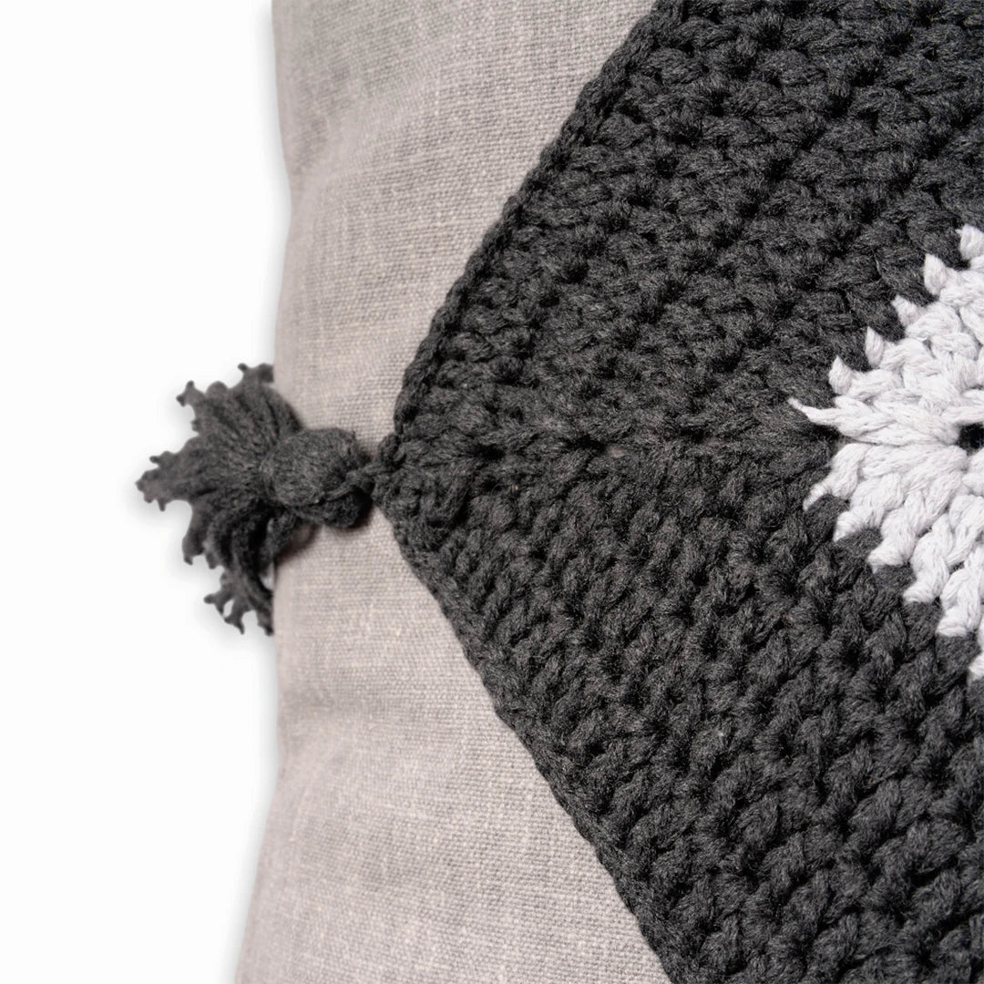 Close-up of the charcoal crochet trim and knotted tassel on the linen evil eye cushion