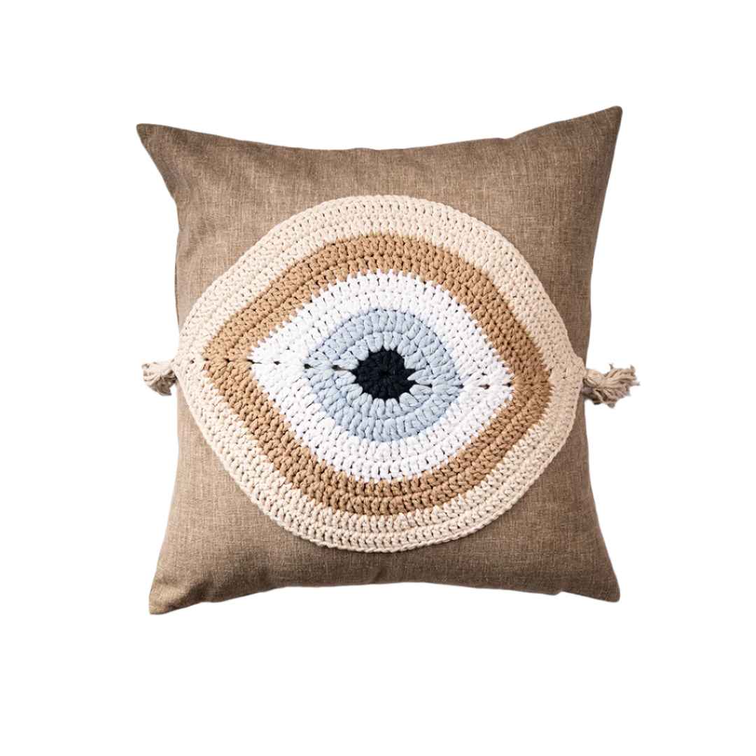 Taupe linen cushion with a beige and ivory crocheted evil eye and corner tassels