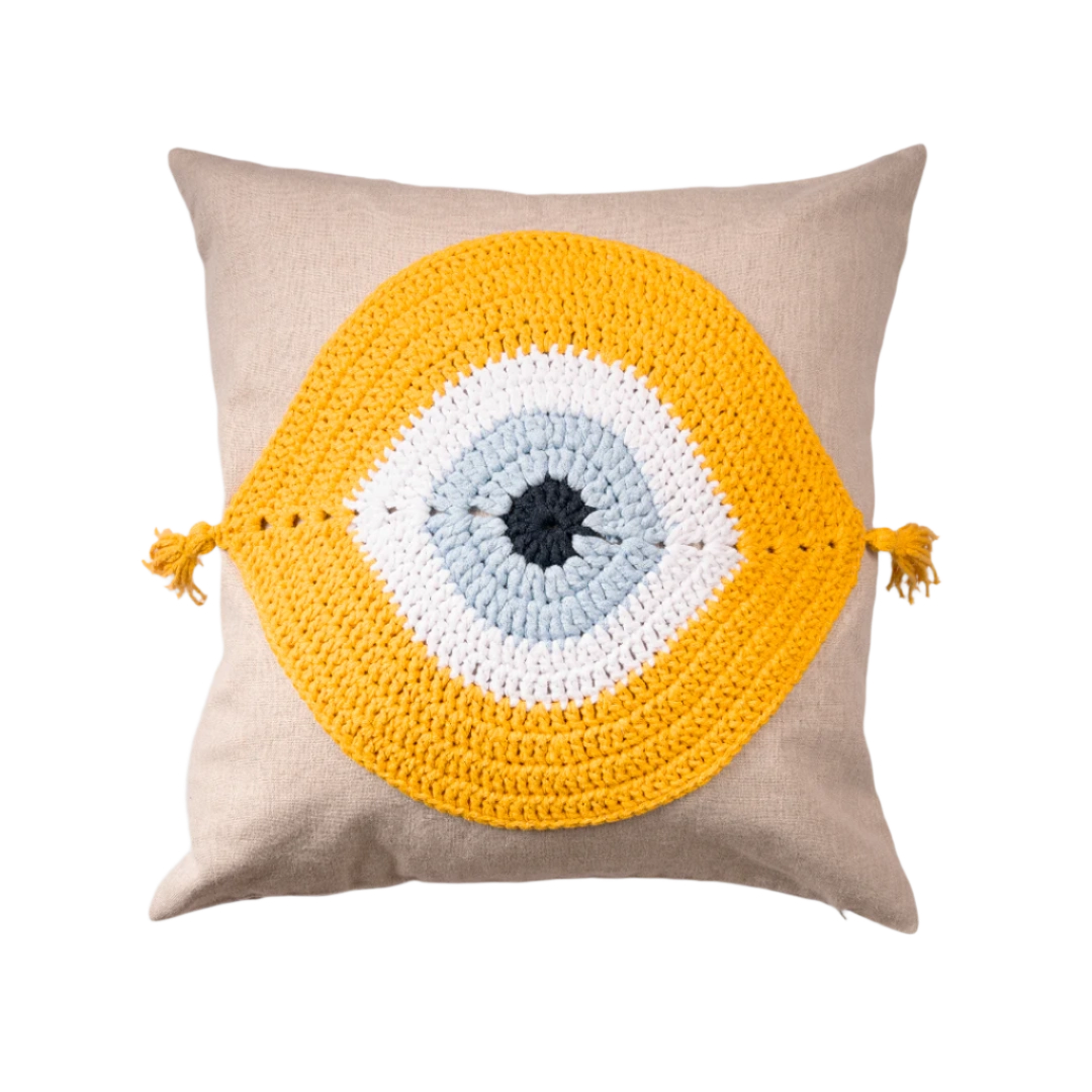 Natural linen cushion with a yellow and ivory crocheted evil eye and corner tassels