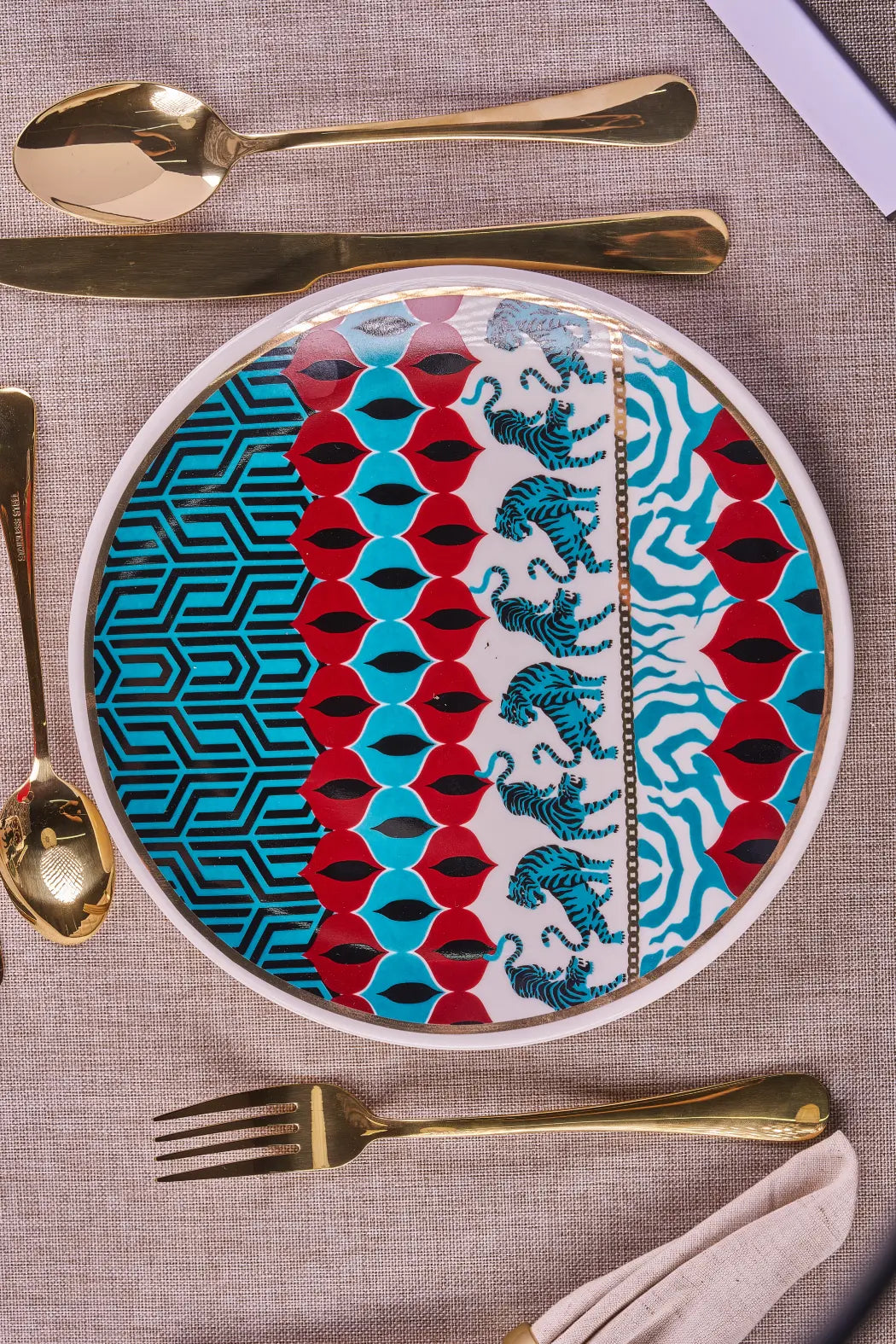 Gatto Wild porcelain plate in a place setting with gold spoons, knife and fork on a linen tablecloth