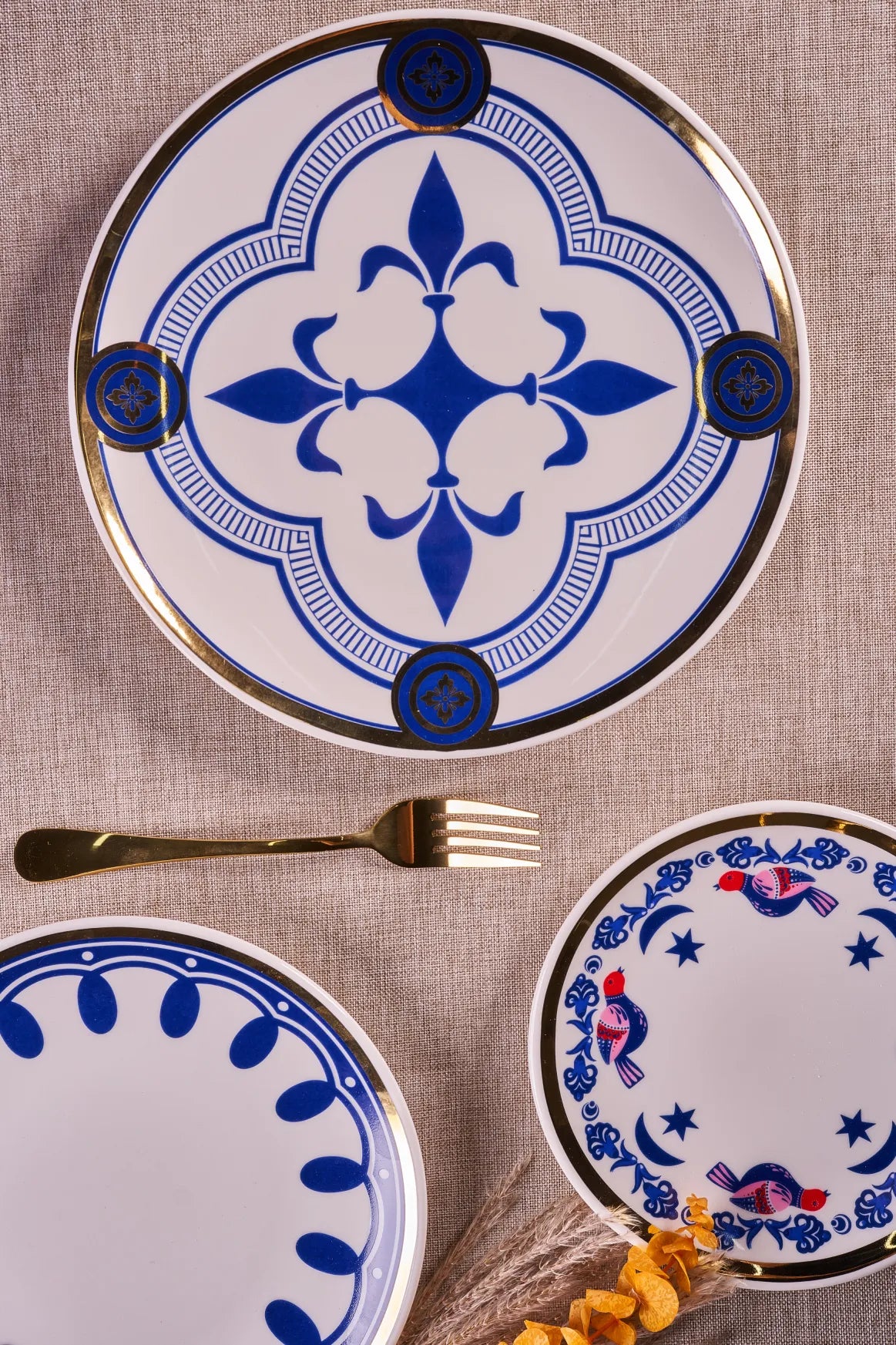 Myth Orient blue and gold porcelain dinner plate from above, with a Myth Mia salad plate and a gold fork on linen