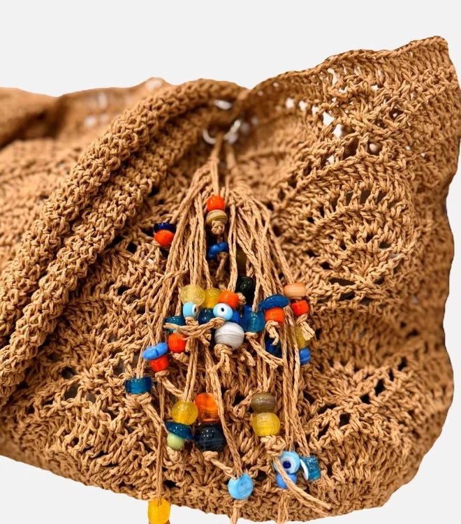 Close-up of the open crochet raffia weave and beaded tassel charm on the Cristina tote