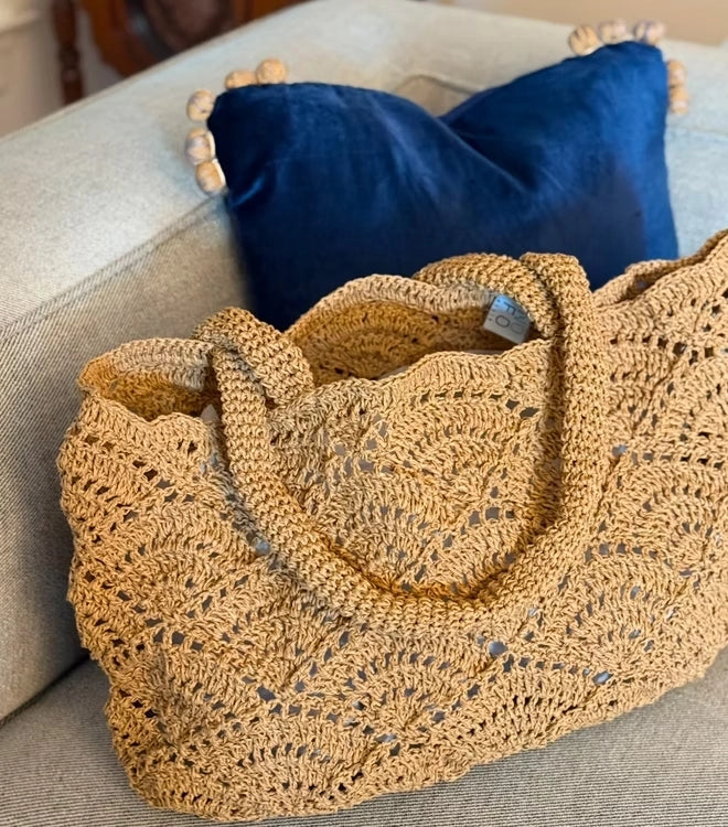 Cristina raffia tote resting on a cream sofa with a blue cushion