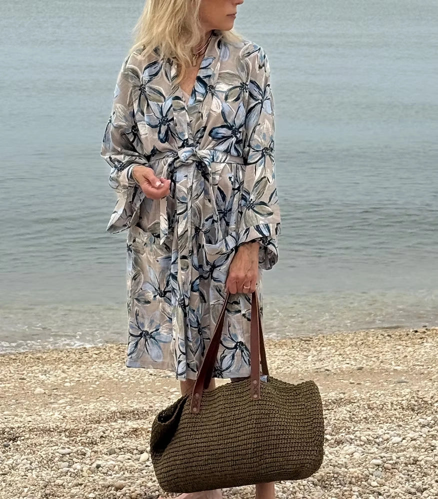 Woman in a floral dress carrying the Fall Green raffia tote along the shoreline